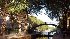 Un canal avec un pont, des arbres et le reflet de bâtiments.