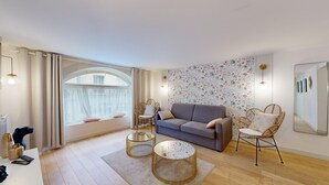 A modern living room with a grey sofa, wicker chairs, a round coffee table, and a large window with curtains.