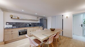 A modern kitchen with a wooden table and chairs, a built-in oven, and a refrigerator.