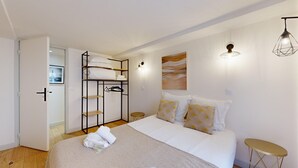 A bedroom with a bed, a wardrobe, a small table, and a wall-mounted light fixture.