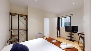 Ein modernes Hotelzimmer mit einem großen Bett, einem Fernseher, einem Schreibtisch und einem Kleiderschrank.