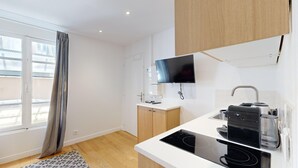 A modern kitchen with a built-in stove, a coffee machine, and a flat-screen TV mounted on the wall. - TBS 16 - Elegant studio in Montorgueil district (Paris)