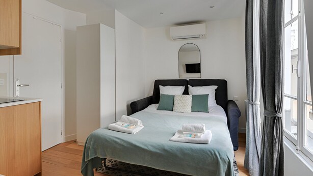 A hotel room with a bed, a small desk, a wardrobe, and a window with curtains. - TBS 16 - Elegant studio in Montorgueil district (Paris)