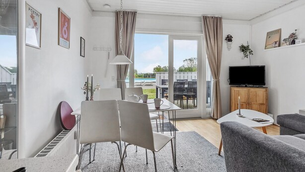 Una sala de estar moderna con comedor, televisor y vistas a una piscina y follaje.