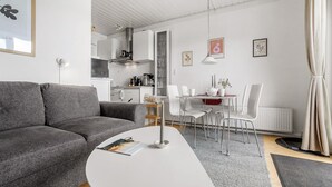 Una sala de estar moderna con un sofá gris, una mesa de centro blanca y un comedor con sillas blancas y una mesa roja.