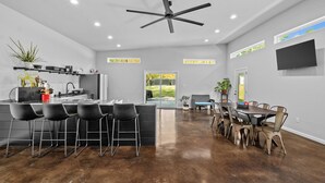Una cocina moderna con una isla central, taburetes negros y una zona de comedor con una mesa grande y sillas.