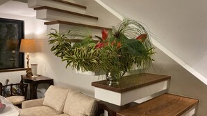 Ein modernes Wohnzimmer mit Treppe, einer Couch, einem Couchtisch und einer großen Kübelpflanze.