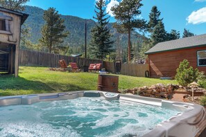 A hot tub in a backyard with a wooden cabin, a wooden fence, and a mountain backdrop. - Potter's Peak (Cascade)