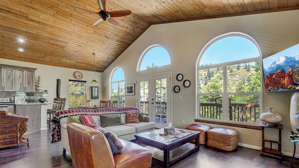 A spacious living area with a high ceiling, wooden beams, and large arched windows offering views of a mountainous landscape. - Potter's Peak (Cascade)