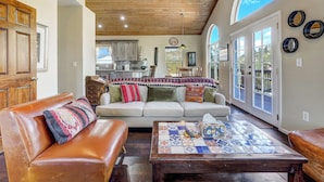 A spacious living room with a leather couch, a coffee table, and a view of the kitchen and outdoor patio. - Potter's Peak (Cascade)