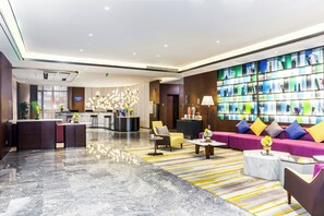 Un moderno vestíbulo de hotel con una recepción, zona de estar y una estantería.