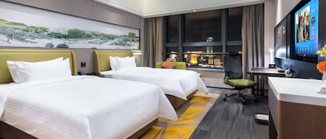 Habitación de hotel con dos camas, un escritorio, una silla, un televisor y un ventanal con vistas a la ciudad.