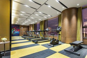 Un gimnasio con cintas de correr, elíptica y bicicleta estática, con piso a cuadros y ventanas amplias.