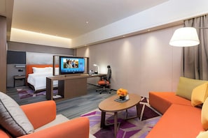 A hotel room with a bed, a desk with a computer, a television, and orange seating. - Hampton Hilton Xuzhou Yunlong Mountain (Xuzhou)