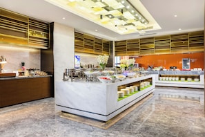 A modern hotel lobby with a marble reception desk, a buffet area with various food items, and a large digital screen displaying content. - Hampton Hilton Xuzhou Yunlong Mountain (Xuzhou)