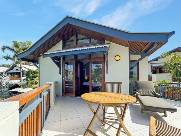 A modern house with a balcony, a round wooden table, and a lounge chair.