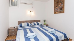 Un dormitorio con cama, mesitas de noche, aire acondicionado de pared, una ventana pequeña e iluminación de pared.