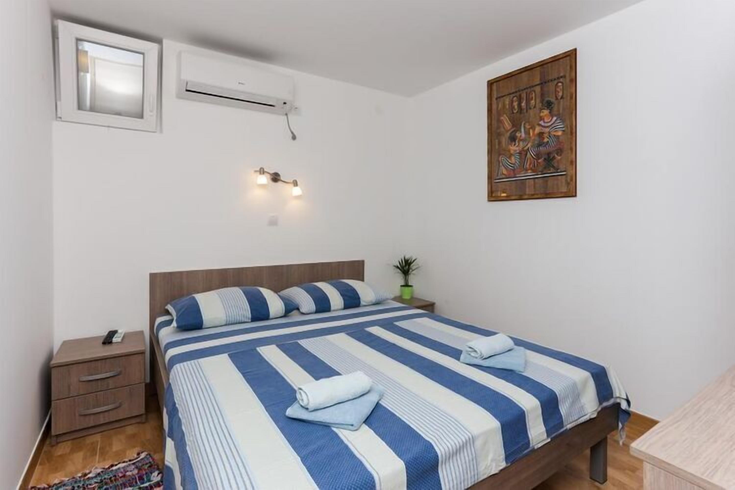 A bedroom with a bed, bedside tables, an air conditioning unit, wall-mounted lights, and a painting.