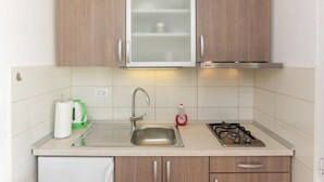 Una cocina con armarios de madera, un lavamanos de acero inoxidable, una tetera y una estufa a gas.