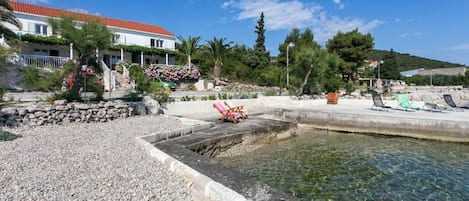 A coastal hotel with a clear pool, stone pathway, and beach chairs.