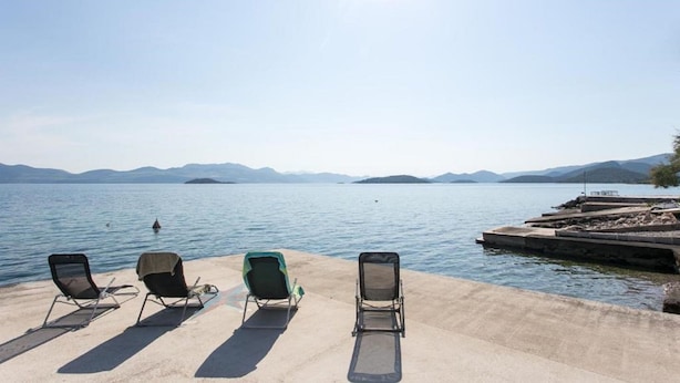 A concrete pier with four lounge chairs facing a calm lake, surrounded by mountains.