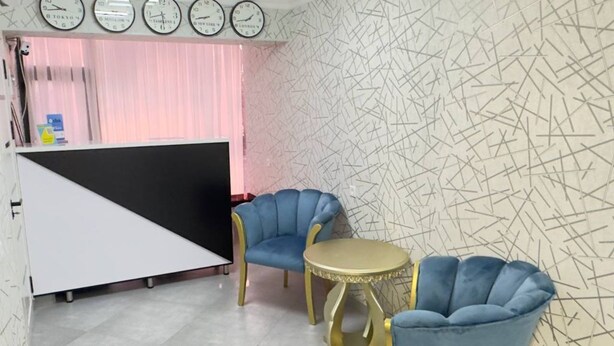 A room with a white partition, two blue armchairs, a round gold table, and a wall clock. - Parvona Hostel (Tashkent)