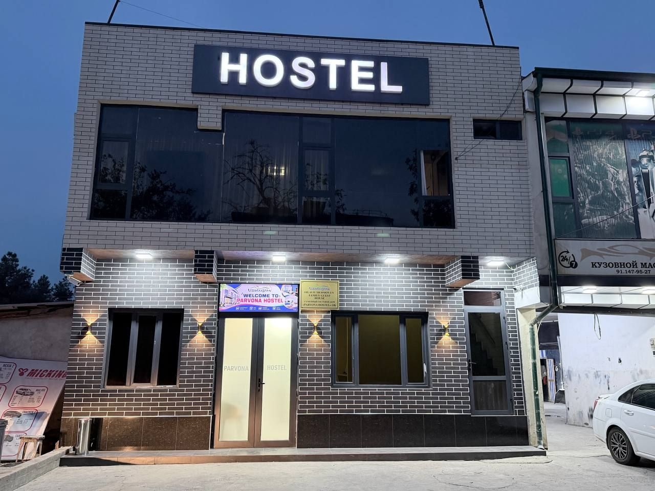 Edificio de un hostal con un llamativo letrero que dice 'HOSTEL', un cartel de bienvenida y un número de contacto.