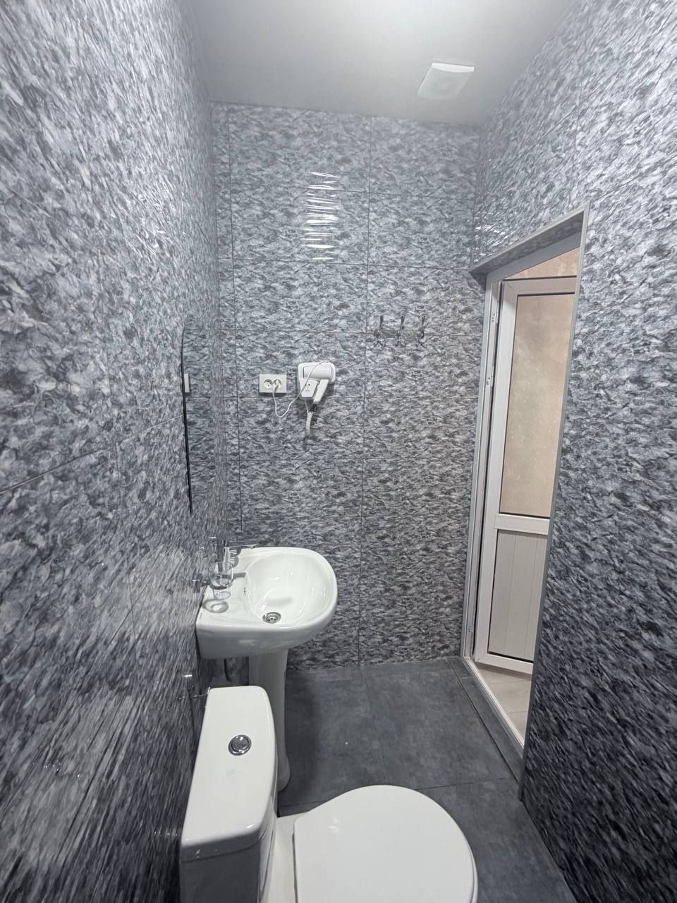 A bathroom with a toilet, sink, and shower area, featuring textured walls and a door leading to another room.