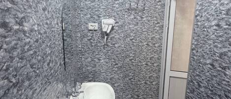 A bathroom with a toilet, sink, and shower area, featuring textured walls and a door leading to another room.