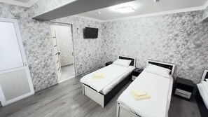 A hotel room with two beds, a TV, and a wardrobe. - Parvona Hostel (Tashkent)