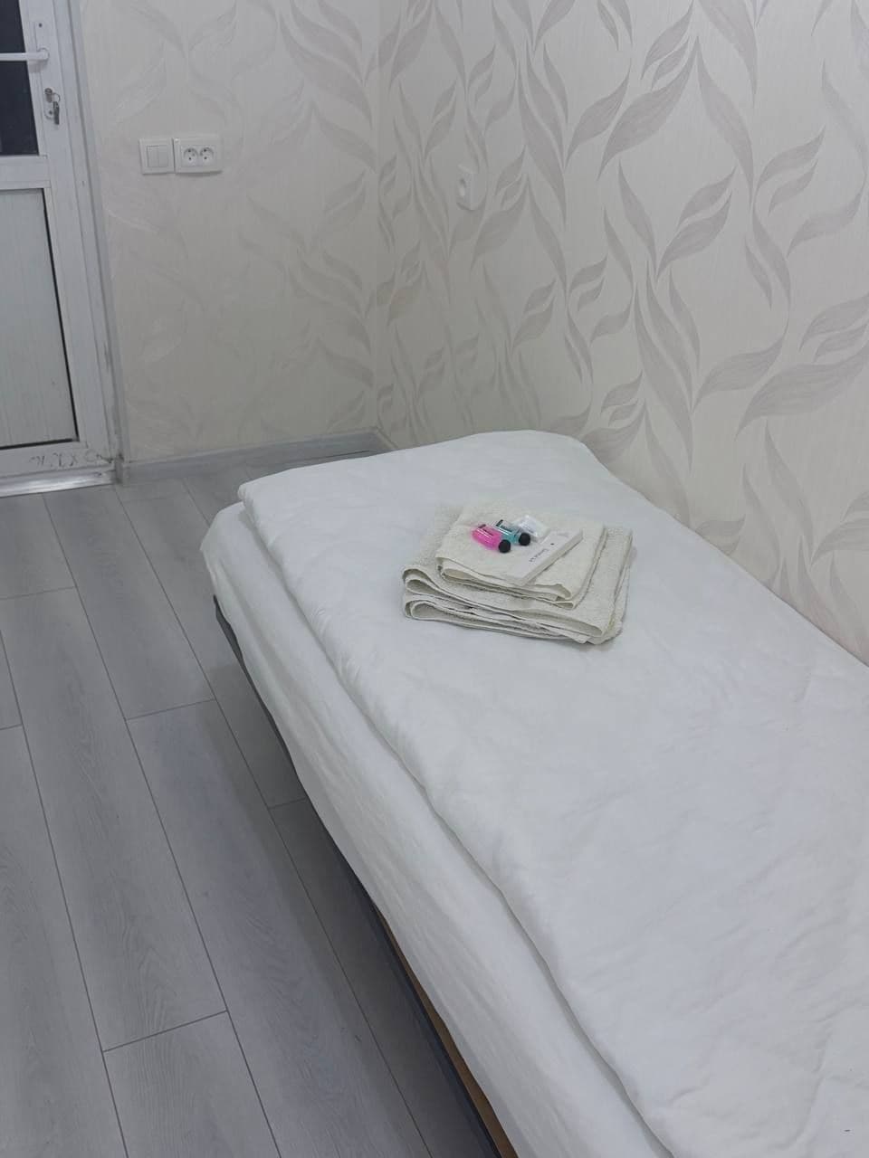 A single bed with a folded white towel and toiletries on it.