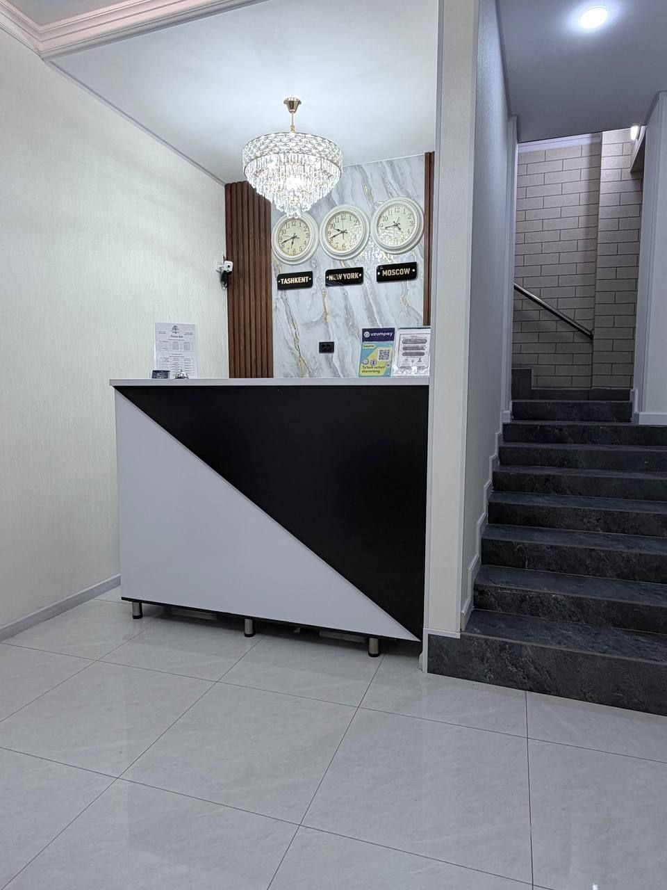 A reception area with a reception desk, a chandelier, clocks, and a staircase.