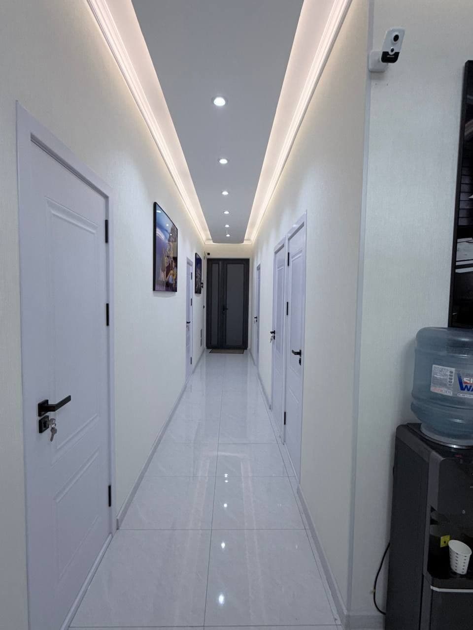 A hallway with white doors, recessed lighting, and a water dispenser on the right.