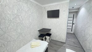 A modern bathroom with a marble wall, a mounted TV, a small sink with a bench, and a towel on the floor. - Parvona Hostel (Tashkent)