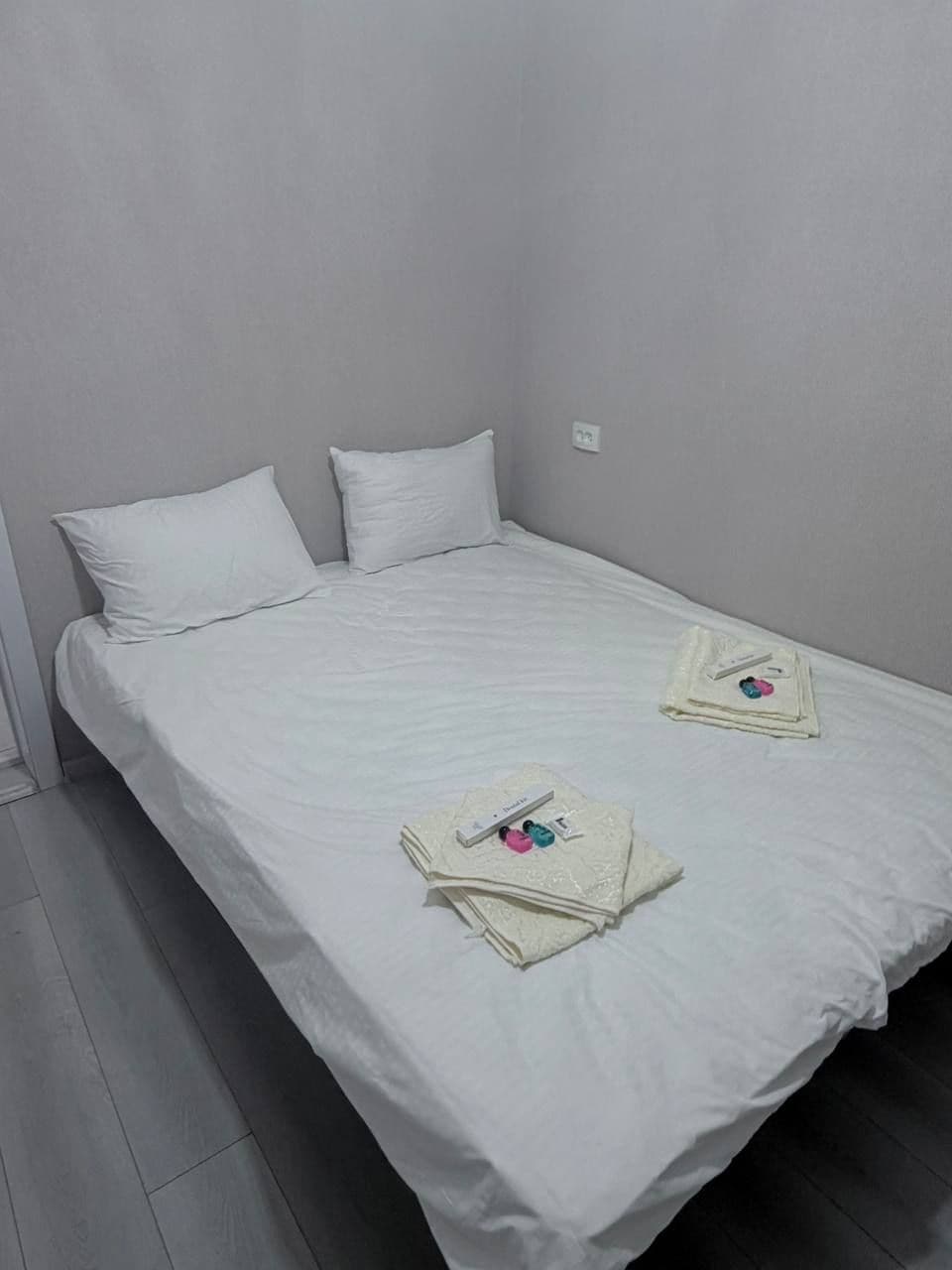 A single bed with white bedding, two pillows, and a folded towel with toiletries on the bed.