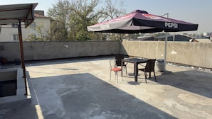 A rooftop patio with a table and chairs, a Pepsi-branded umbrella, and a concrete floor. - Parvona Hostel (Tashkent)