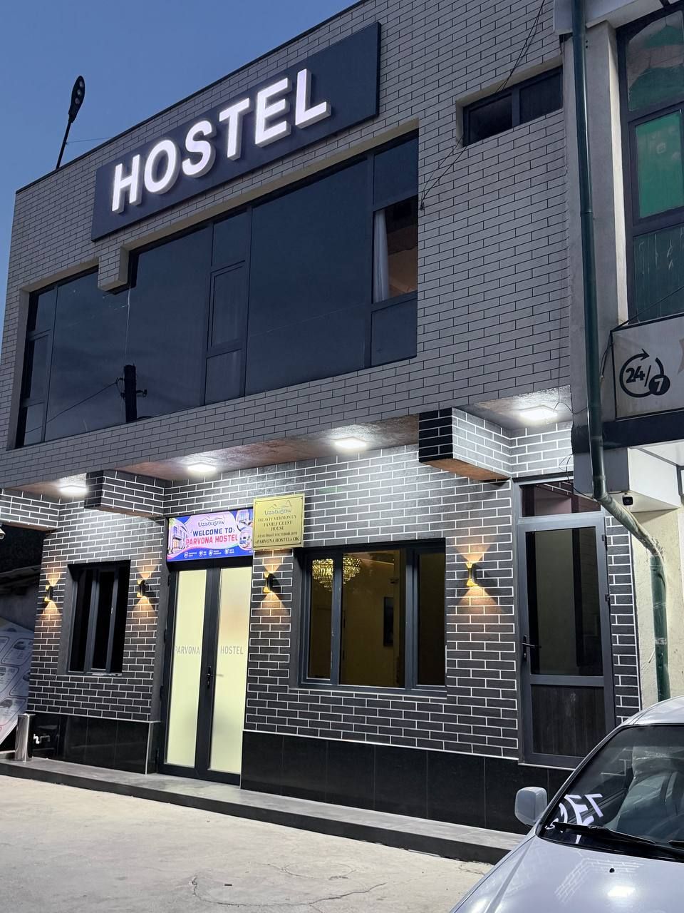 Um hostel com uma placa grande com a palavra 'HOSTEL', um letreiro de boas-vindas e o símbolo de serviço 24 horas.