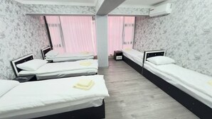 A hotel room with three single beds, a wooden floor, and a large window with pink curtains. - Parvona Hostel (Tashkent)
