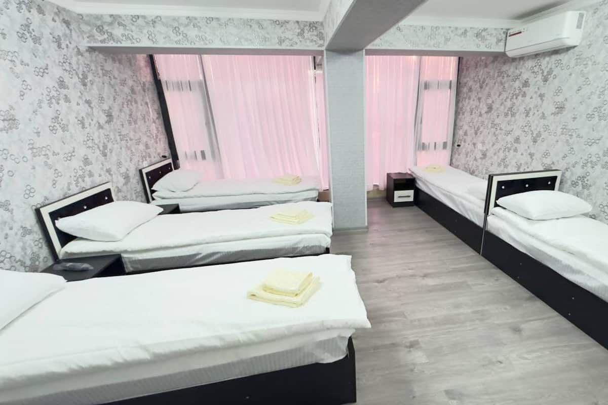 Habitación de hotel con tres camas individuales, suelo de madera y un amplio ventanal con cortinas rosadas.