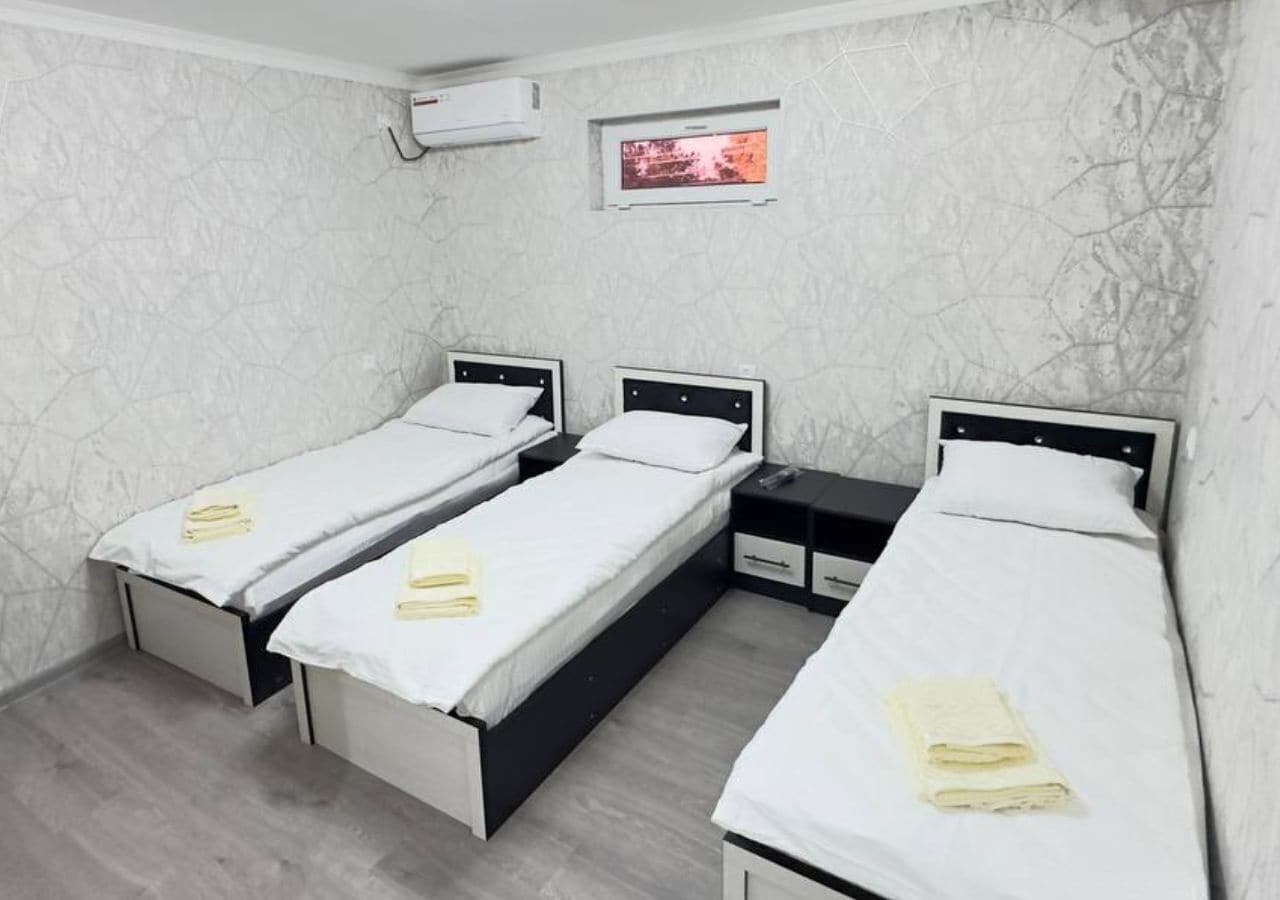 A hotel room with three single beds, each with a white mattress and a small bedside table.