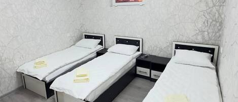 A hotel room with three single beds, each with a white mattress and a small bedside table.