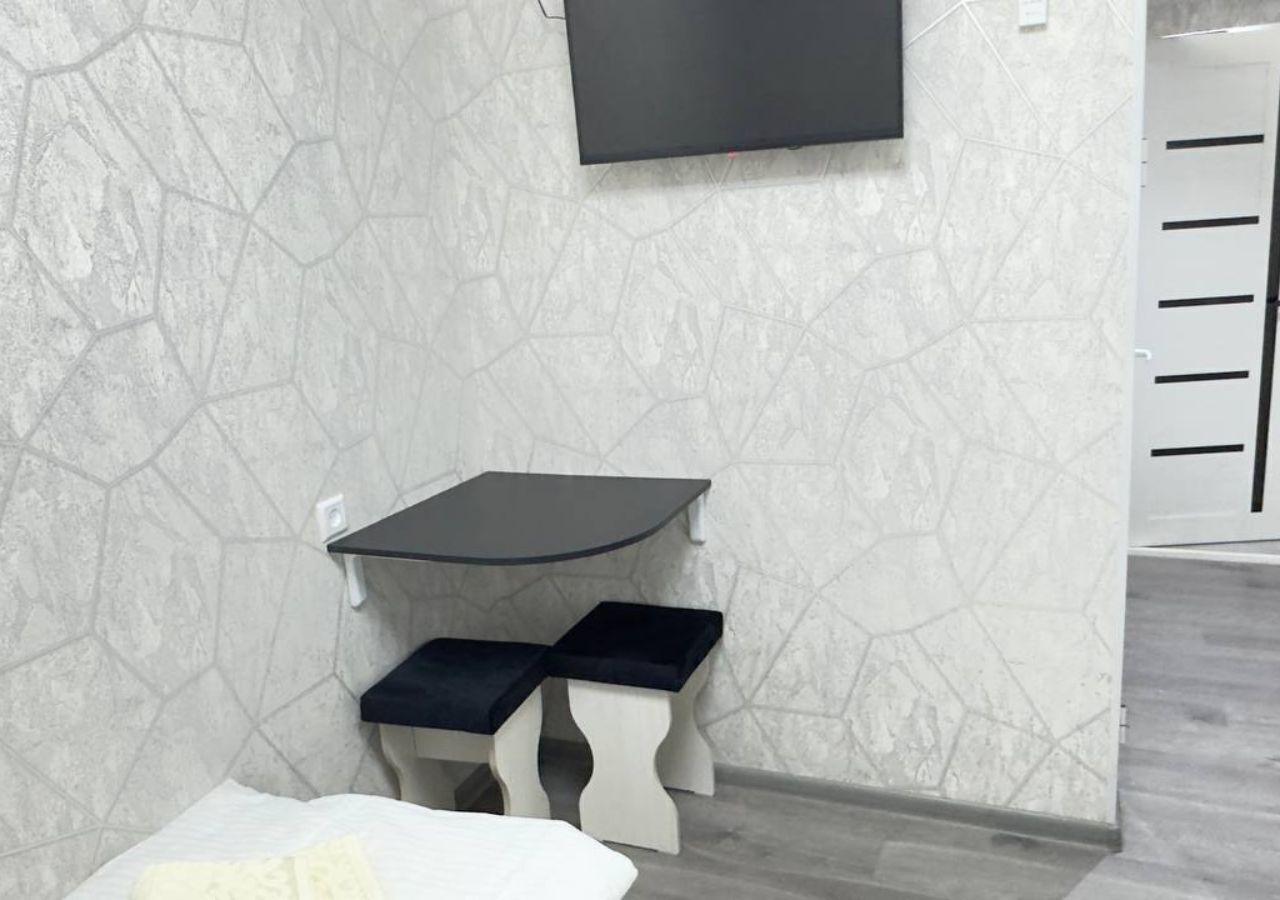 A room with a white bed, a small white table with a black top, and a black bench.