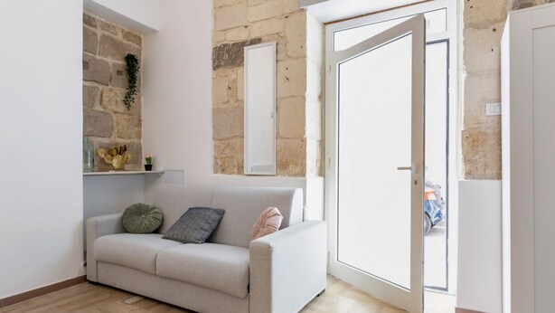 Een woonkamer met een bank, een stenen muur en een schuifpui naar buiten.