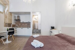 Quarto de hotel com cama, secretária, cadeira, mesa pequena, cozinha compacta e banheiro.