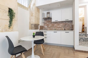 A compact kitchen with white cabinets, a tiled backsplash, and a small dining area with a round table and two chairs.