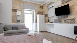 Een slaapkamer met een stenen muur, een flatscreen televisie, een sofa, een bed en een kledingkast.