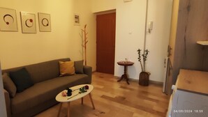 A living room with a sofa, a small table with a rose, and a plant.
