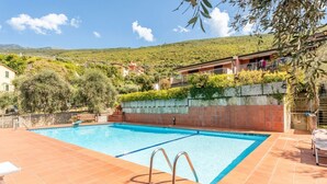 A swimming pool with a view of a hillside, a wooden bench, and a stone wall.