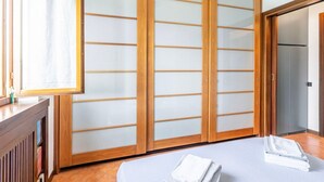 A room with a sliding shoji screen door, a bed with neatly folded towels, and a wooden cabinet with books.