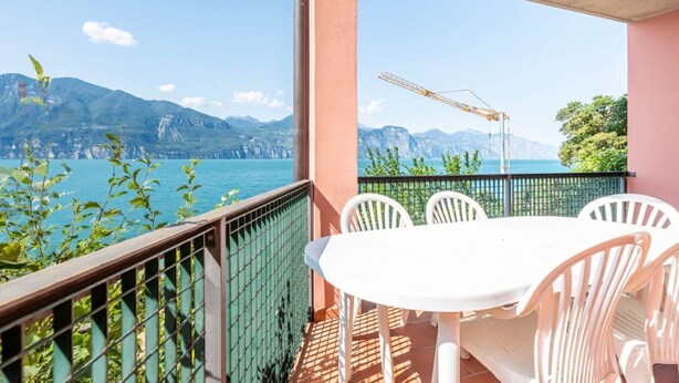 A balcony with a table and chairs, overlooking a mountainous coastline.